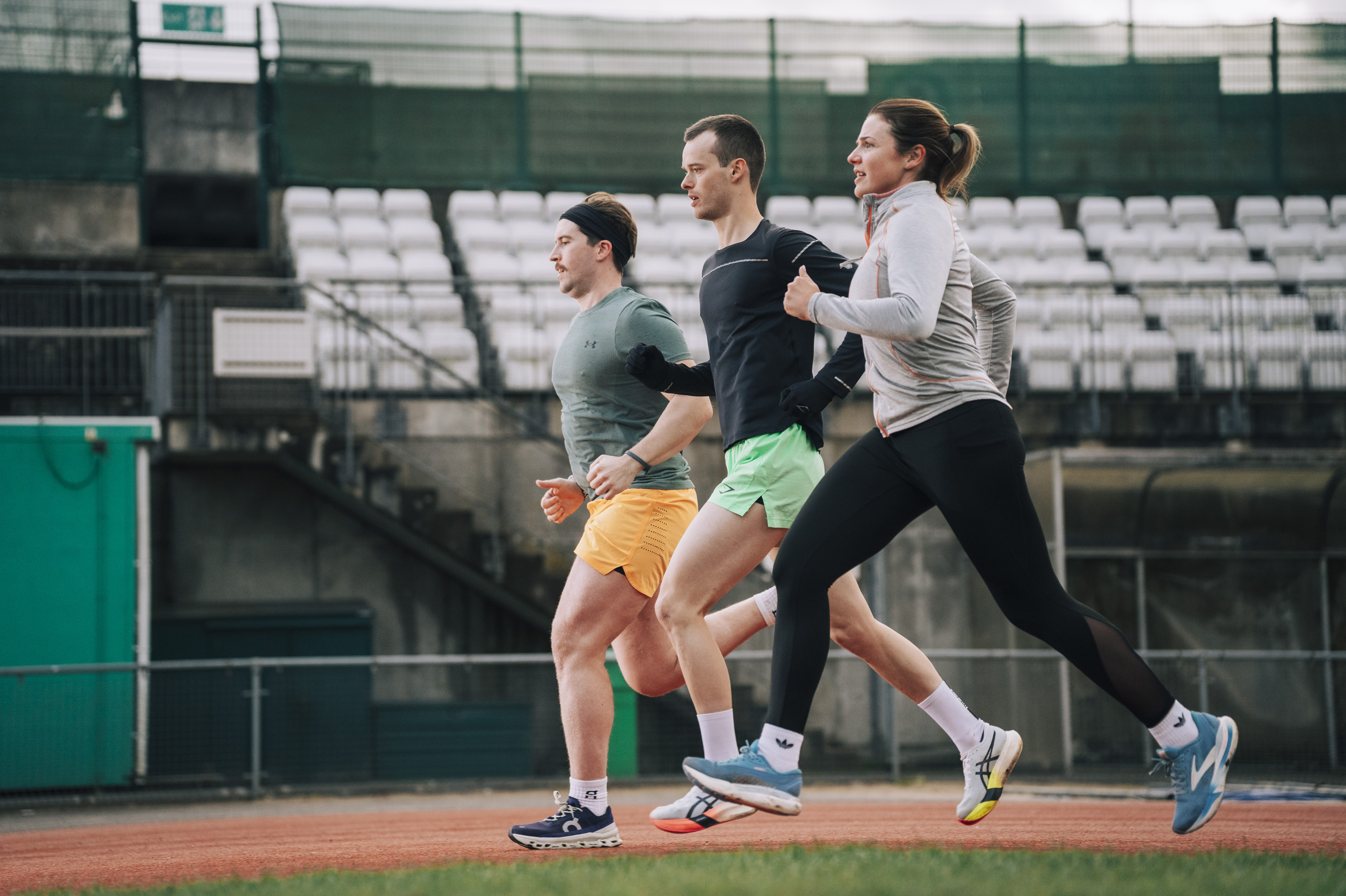 Three athletes running together on a track.